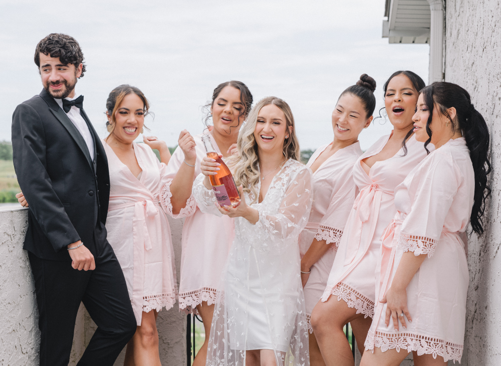 bridesmaids in pink robes popping champagne
