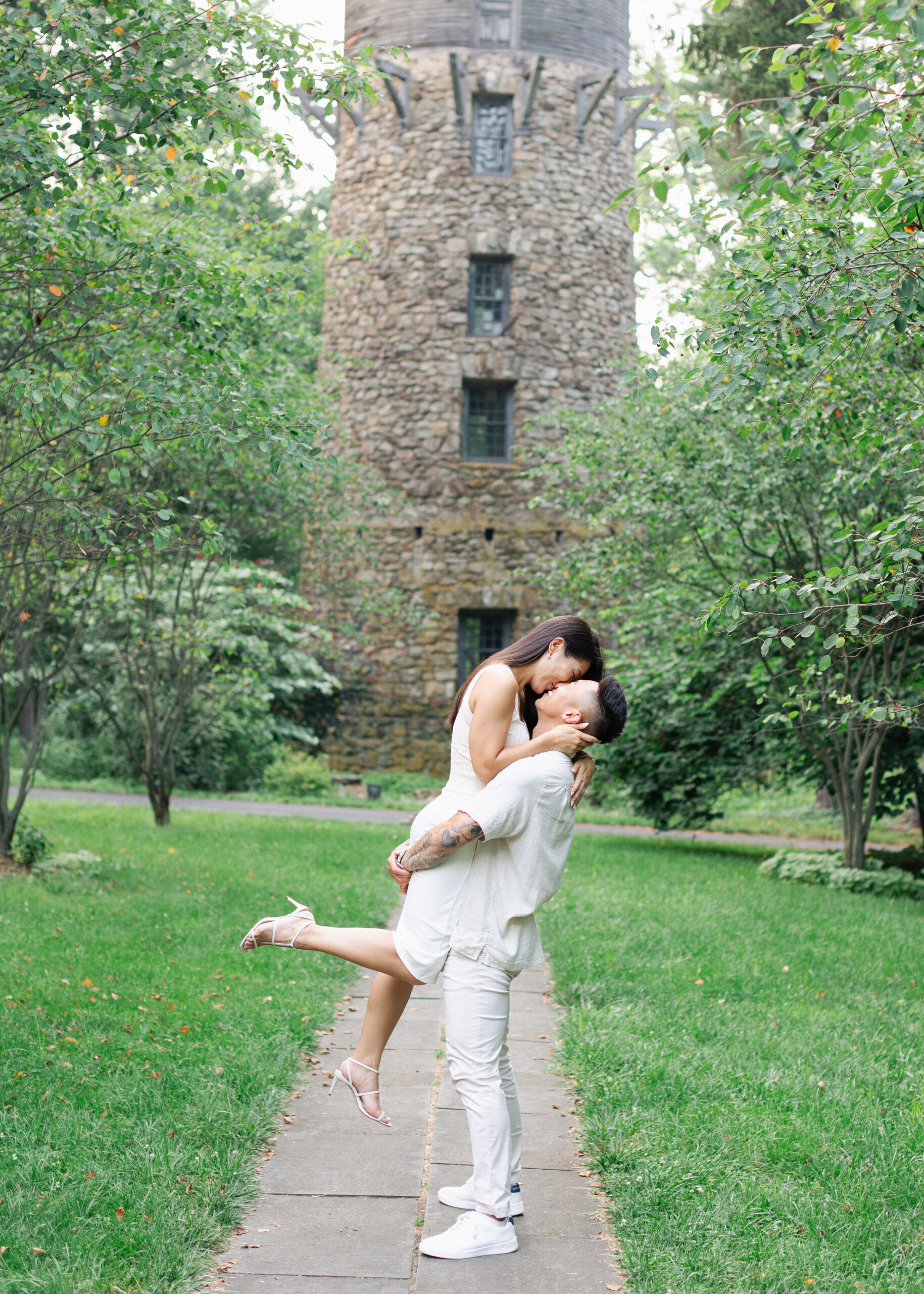 engaged couple lifting up girl in front of stone tower garden