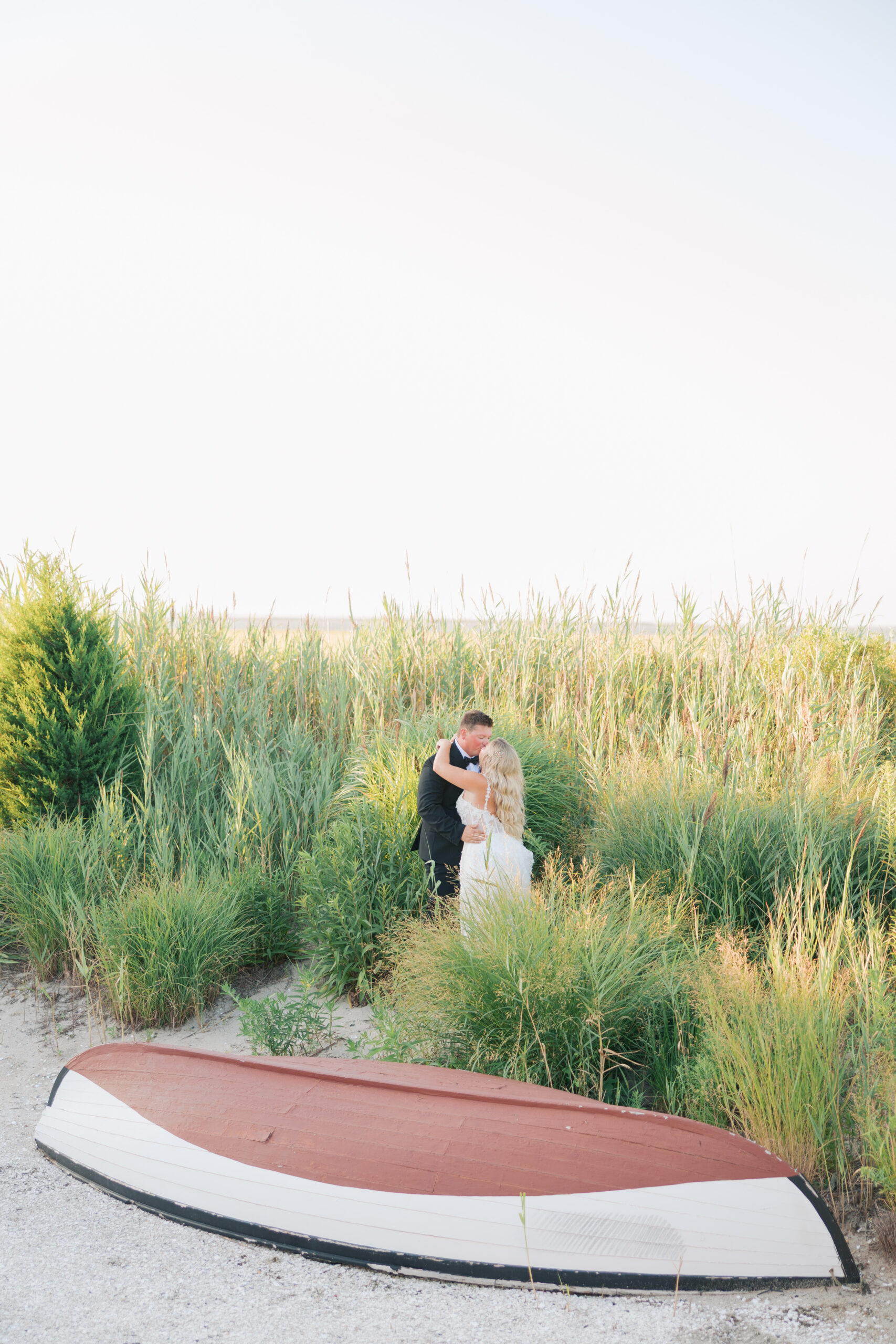 Wedding couple in the reeds by an overturned boat behind Bonnet Island Estate at sunset